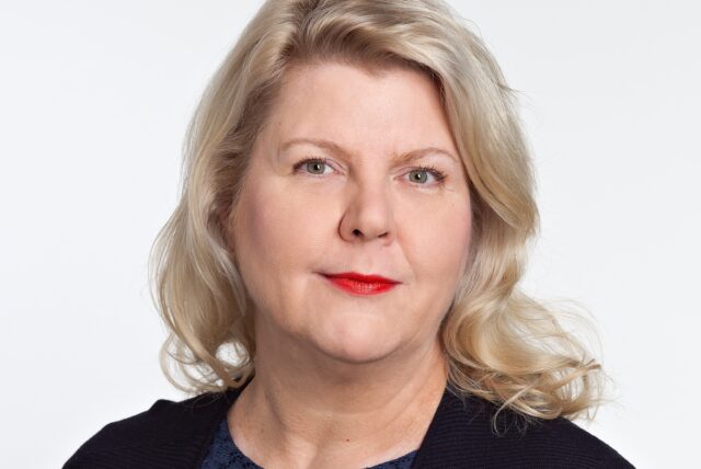 Kasvokuvassa vaaleatukkainen, vakavailmeinen tummaan asuun pukeutunut nainen.