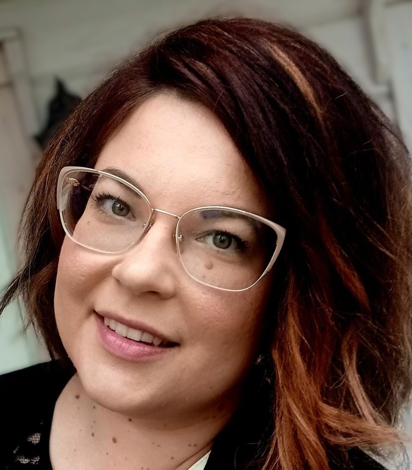 Tummatukkainen simälasipäinen nainen tiukasti rajatussa kasvokuvassa