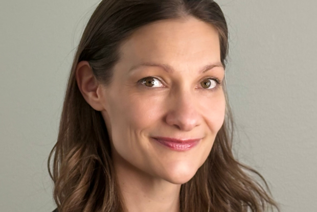 Ruskeatukkainen hillitysti hymyilevä nainen tiukasti rajatussa kasvokuvassa.