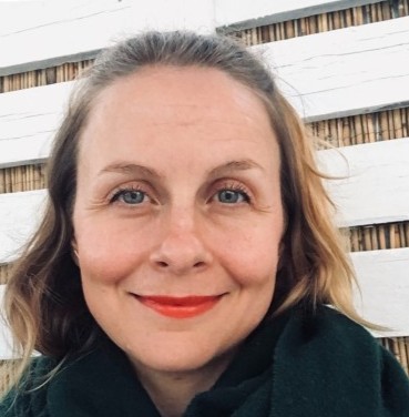 Hymyilevä ruskeatukkainen naisoletettu tiukasti rajatussa kasvokuvassa.