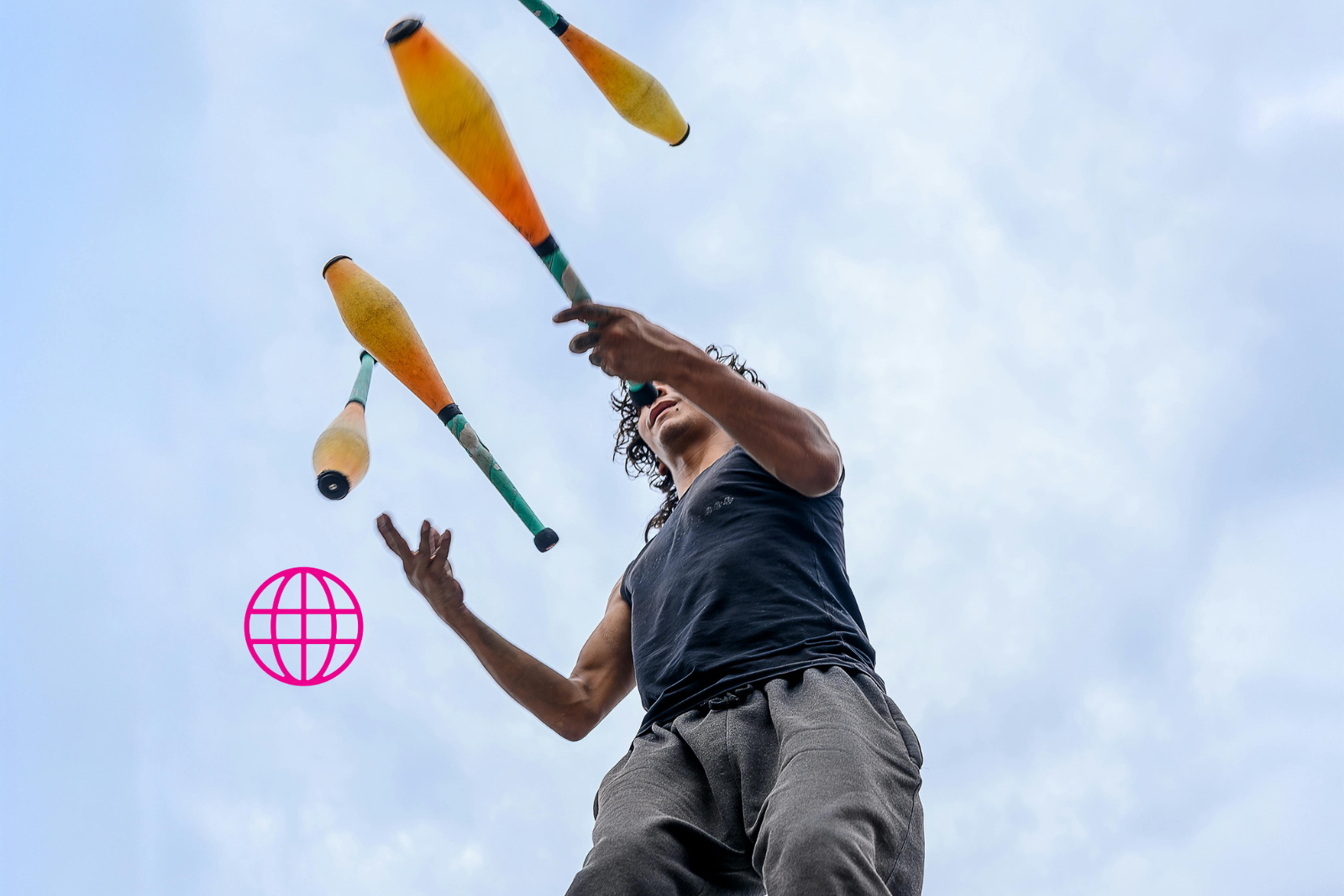 Nuori miesoletettu jonglöörää vaaleansinistä taivasta vasten.